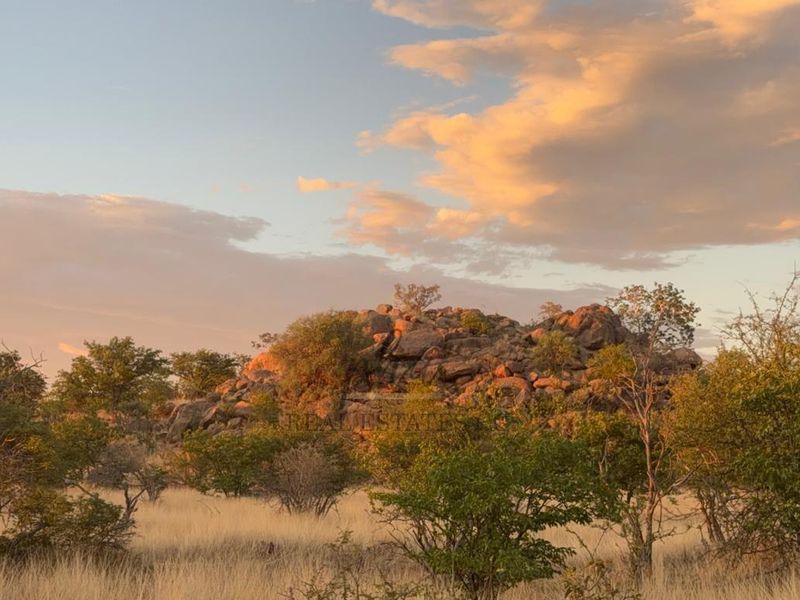A scenic view of the natural landscape featuring rocky outcrops and indigenous vegetation under a sunset sky.