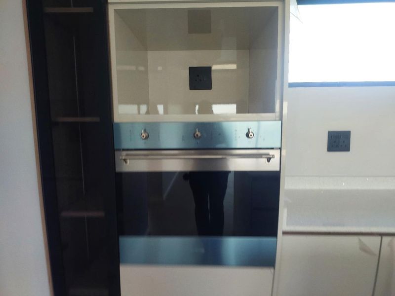 A modern kitchen featuring a built-in oven, sleek cabinetry, and stone countertops with integrated electrical outlets.