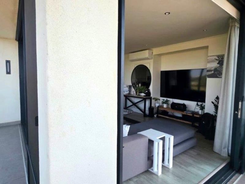 An open-plan living area featuring modern tiled flooring, recessed lighting, and an air conditioning unit, with seamless access to a private balcony.