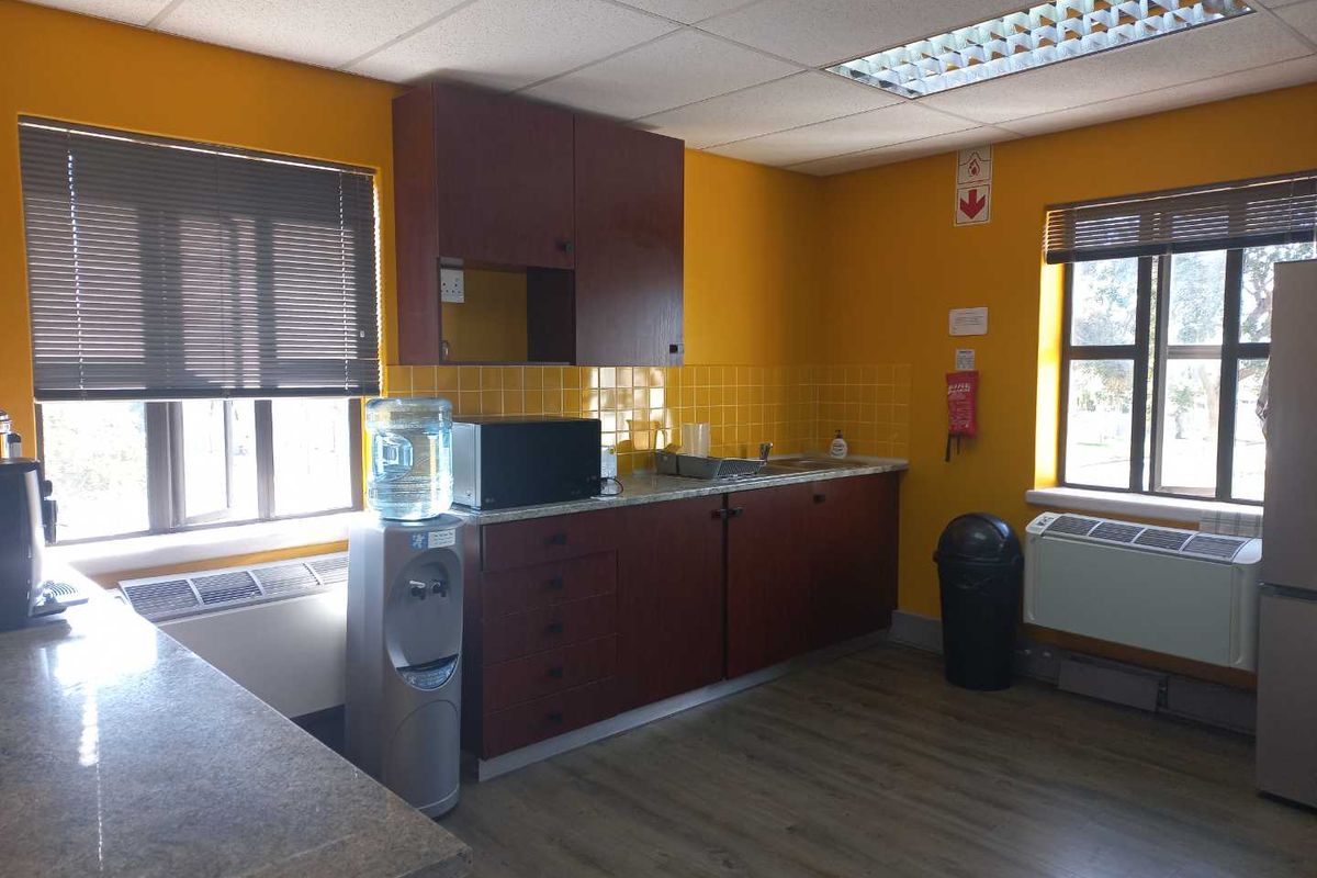 A functional office kitchenette featuring built-in cabinetry, laminate countertops, a stainless steel sink, and tiled splashbacks.