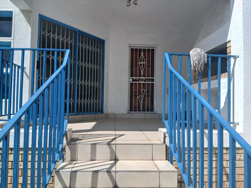 Covered patio area featuring tiled flooring, a built-in braai, and secure metal access points, providing a functional outdoor entertainment space.