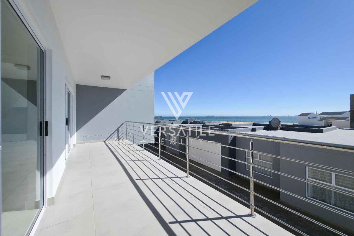 A spacious balcony featuring modern tiled flooring and a stainless steel railing, offering clear views of the ocean and surrounding neighborhood.