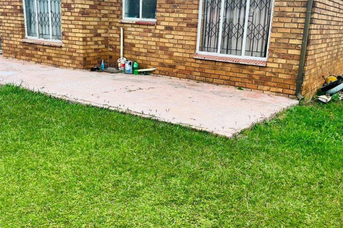 A rear view of a brick house featuring a concrete patio area and a well-maintained lawn.