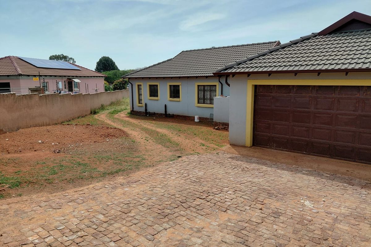 Rear view of the property featuring a tiled roof, garage access, and a large unlandscaped yard area with a cobblestone driveway.