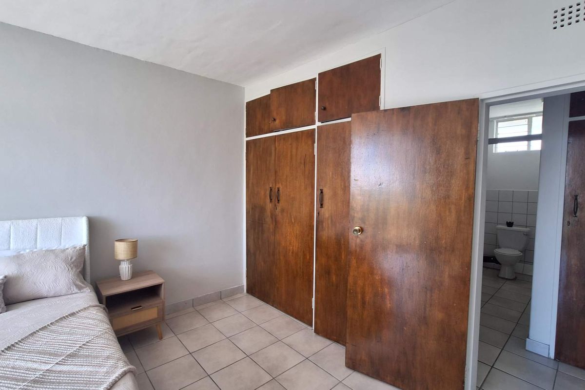 Bedroom featuring tiled flooring and built-in wooden cupboards, with an adjoining bathroom visible through the doorway.