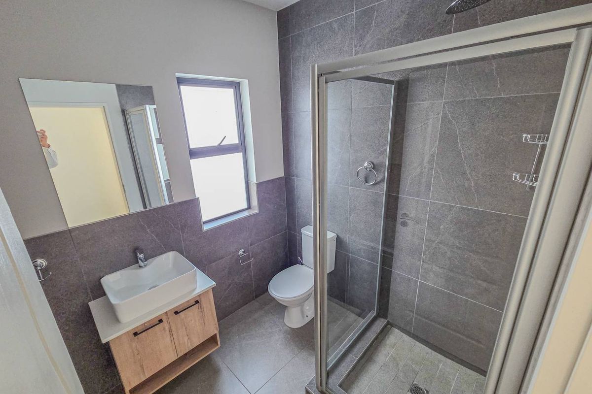 Modern bathroom featuring a vessel sink vanity, a glass-enclosed shower with a rain shower head, and contemporary grey wall and floor tiling.