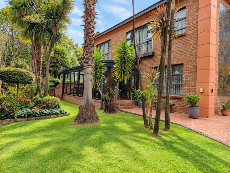 A well-maintained rear exterior view of a double-story brick house featuring a landscaped garden and an enclosed patio area.