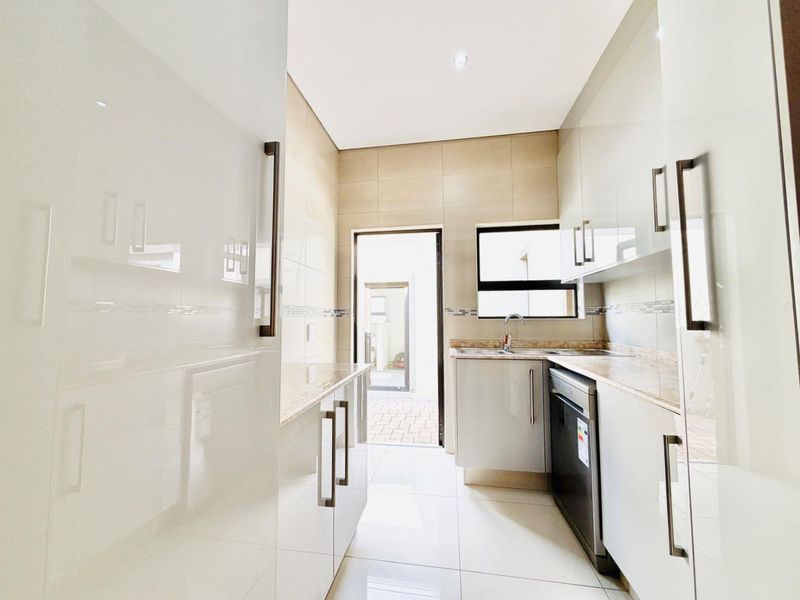A modern, well-maintained scullery featuring sleek built-in cabinetry, stone countertops, a stainless steel sink, and tiled finishes with direct access to an outdoor area.