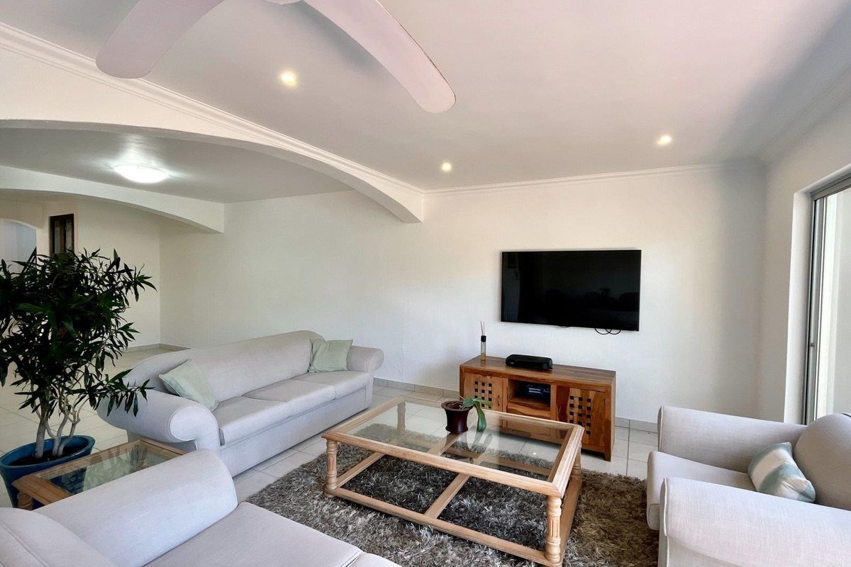 A bright and spacious living room featuring tiled flooring, recessed downlights, a ceiling fan, and an elegant archway leading to adjacent areas.