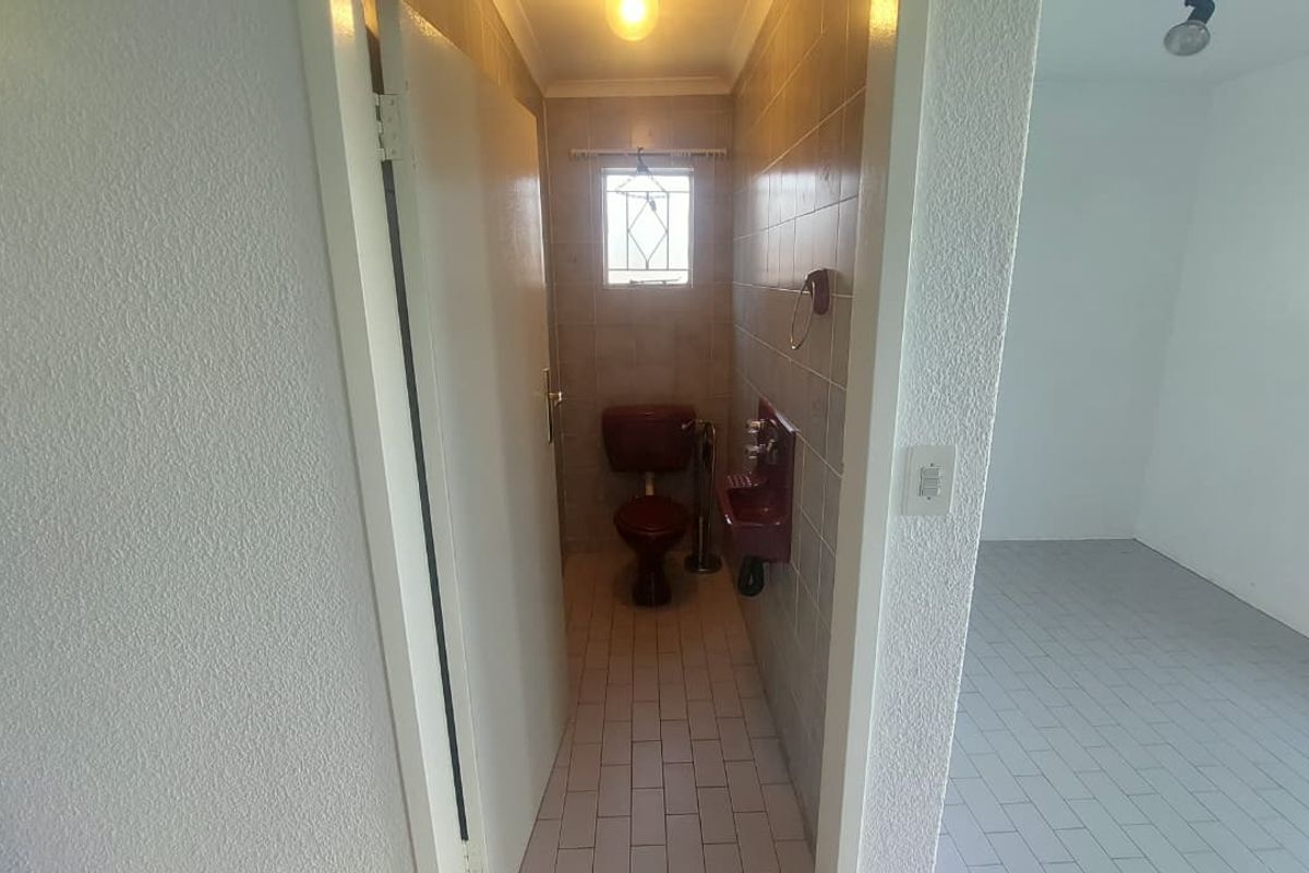 A small, dated bathroom featuring a vintage-style toilet and wall-mounted basin with tiled walls and flooring.