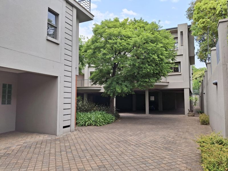 A view of the townhouse complex entrance featuring a paved driveway, covered parking area, and multi-level architectural design with mature landscaping.