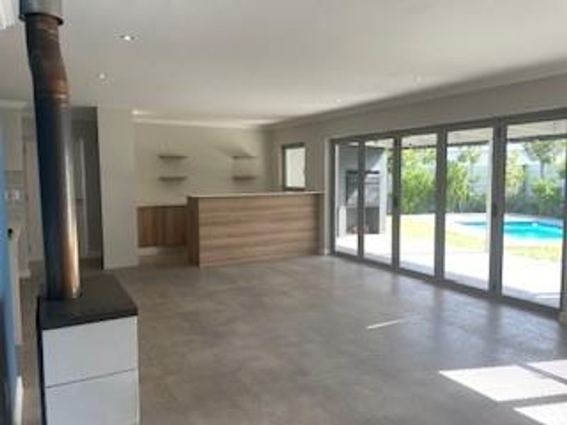Spacious open-plan living area featuring a modern built-in bar, freestanding fireplace, and large stacker doors opening to a pool and patio area.