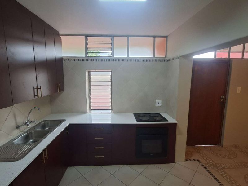 A functional kitchen featuring dark wood cabinetry, a double sink, built-in oven and hob, and tiled finishes throughout.