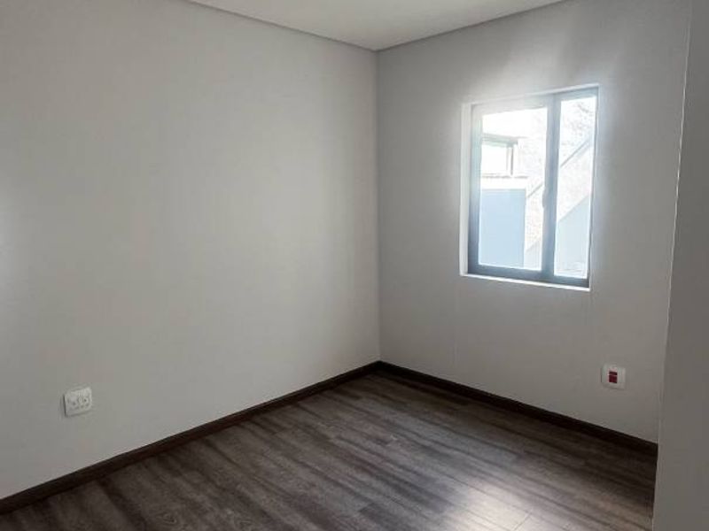 A clean, empty bedroom featuring modern laminate flooring, neutral walls, and adjustable track lighting, offering a versatile space ready for personalization.