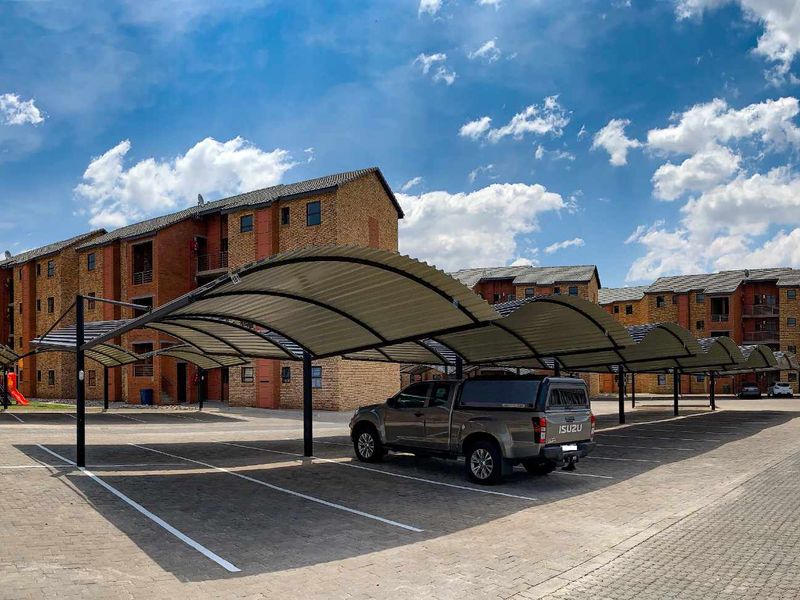 Exterior view of an apartment complex featuring covered parking bays, paved driveway, and communal outdoor space with playground equipment.
