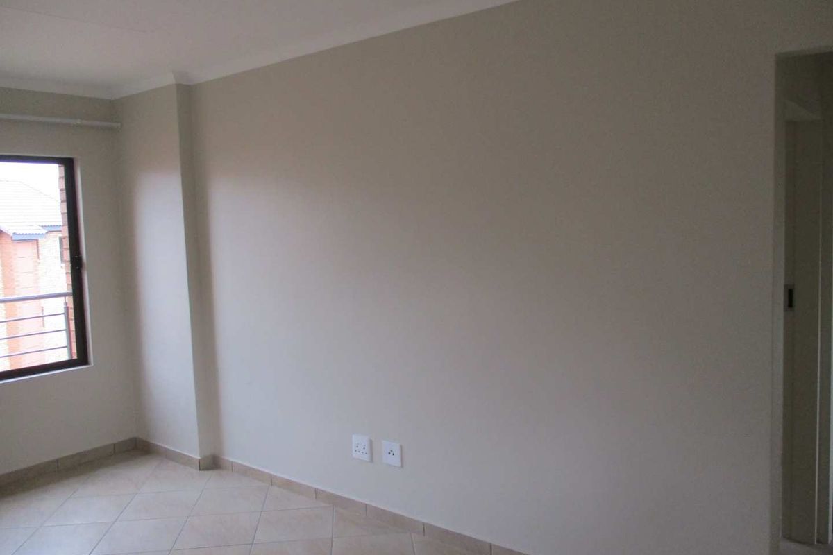 A bright, empty living area featuring neutral wall tones, tiled flooring, and a window providing natural light.