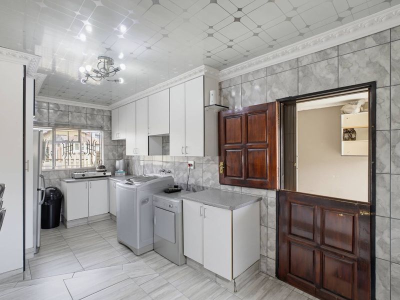 A functional kitchen featuring white built-in cabinetry, tiled walls and flooring, and a distinctive stable-style wooden door leading to an adjacent room.