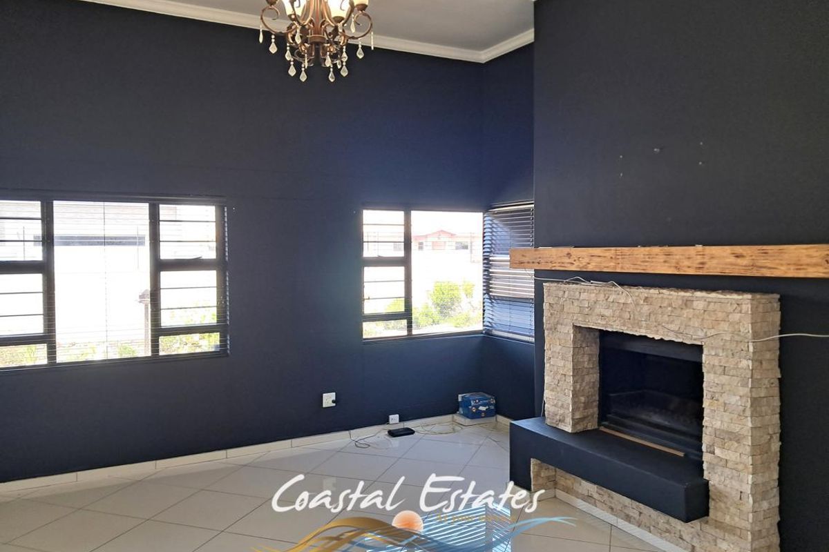 Spacious living room featuring a stone-clad fireplace with a timber mantel, tiled flooring, and large windows providing ample natural light.
