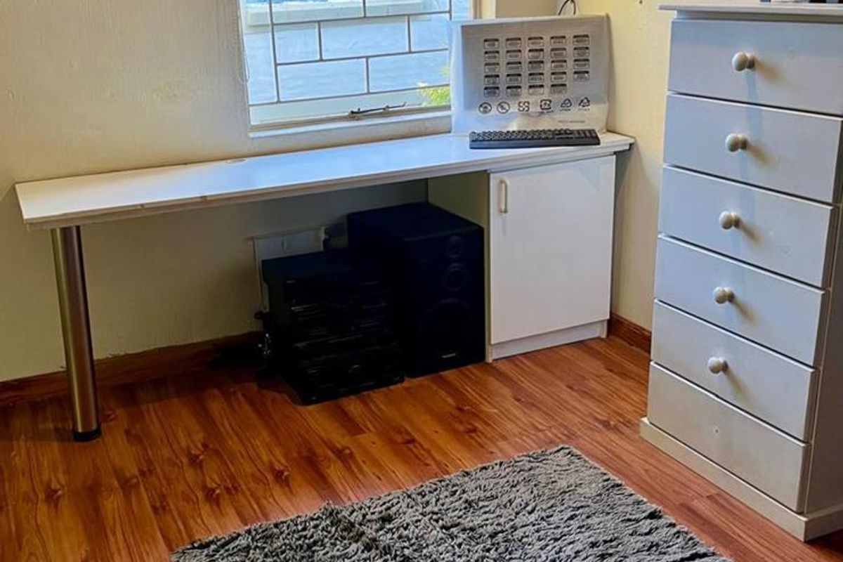 A bedroom featuring wood-look laminate flooring, a built-in desk with storage cabinetry, and a window fitted with security bars.