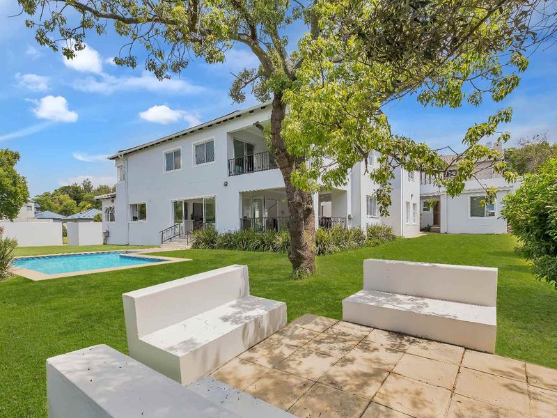 Rear view of the property featuring a well-maintained garden, swimming pool, and a paved patio area with built-in concrete seating.