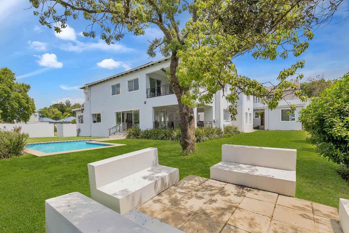 Rear view of the property featuring a well-maintained garden, swimming pool, and a paved patio area with built-in concrete seating.