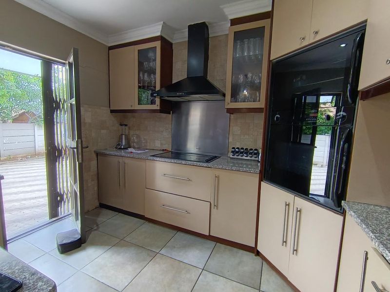 Functional kitchen featuring built-in cabinetry, granite countertops, integrated oven, and hob with extractor fan, providing direct access to the outdoor area.