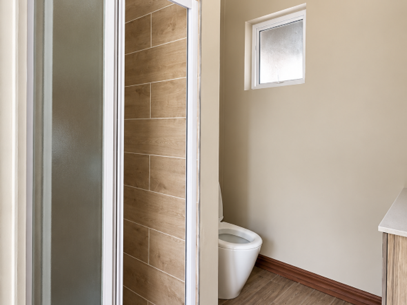 A clean, modern bathroom featuring a walk-in shower with wood-look tiling, a white toilet, and a vanity cabinet with neutral wall finishes.