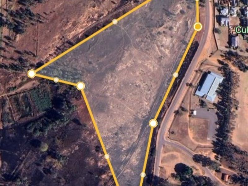 An aerial view of a large, undeveloped land parcel with marked boundaries, situated near a road and residential area.