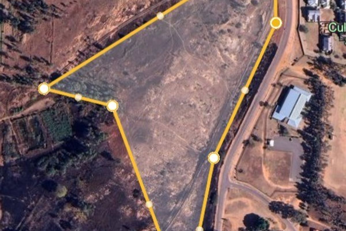 An aerial view of a large, undeveloped land parcel with marked boundaries, situated near a road and residential area.