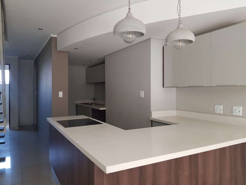 Modern kitchen featuring sleek cabinetry, stone countertops, an integrated electric hob, and contemporary pendant lighting in an open-plan layout.