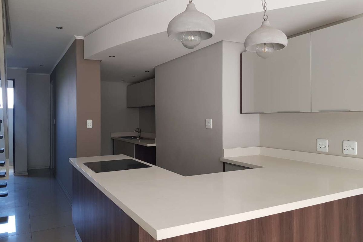 Modern kitchen featuring sleek cabinetry, stone countertops, an integrated electric hob, and contemporary pendant lighting in an open-plan layout.