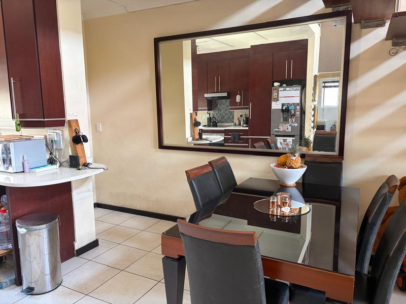 Open plan dining and kitchen area featuring dark wood cabinetry, tiled flooring, and a breakfast counter, reflecting a functional but dated interior space.