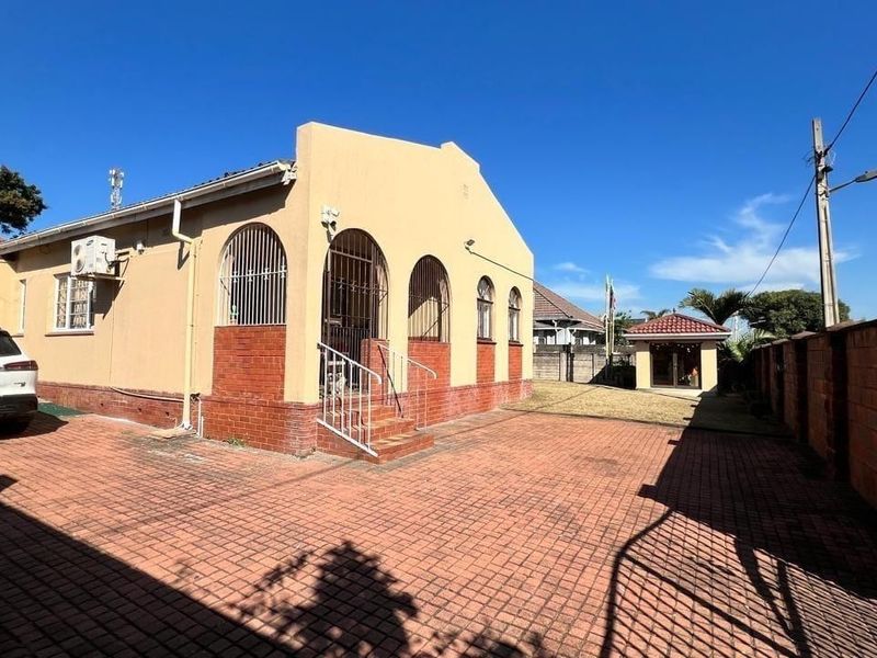 Front exterior view of a house featuring brick paving, arched windows with security bars, and a brick boundary wall.