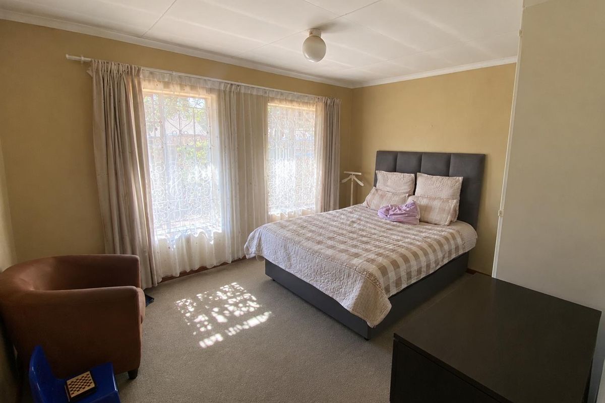 A standard bedroom featuring carpeted flooring, dual windows with security bars, and neutral wall finishes.