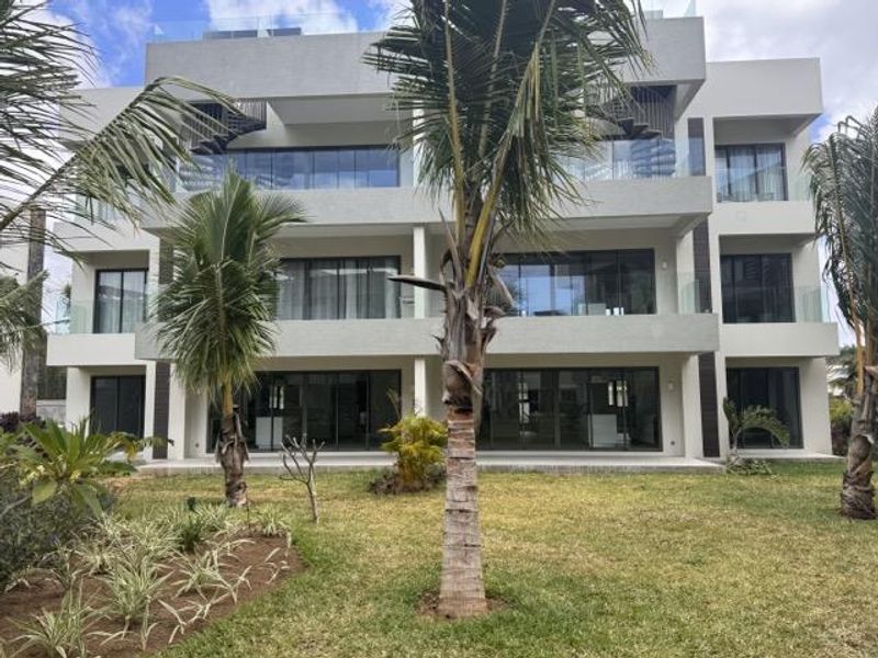Modern multi-story apartment building featuring clean concrete lines, expansive glass sliding doors, and contemporary glass balustrades overlooking a landscaped garden area.