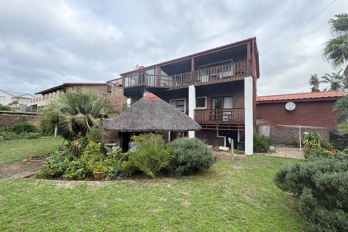 Rear view of a multi-story brick house featuring a thatched lapa, wooden balconies, and a spacious garden area.