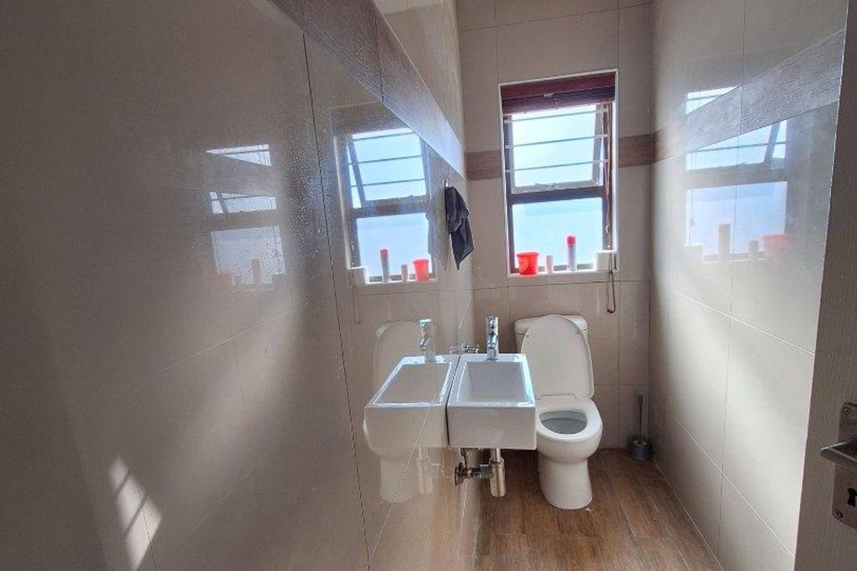 A modern, compact bathroom featuring floor-to-ceiling tiled walls, wood-look floor tiles, a wall-mounted basin, and a toilet.