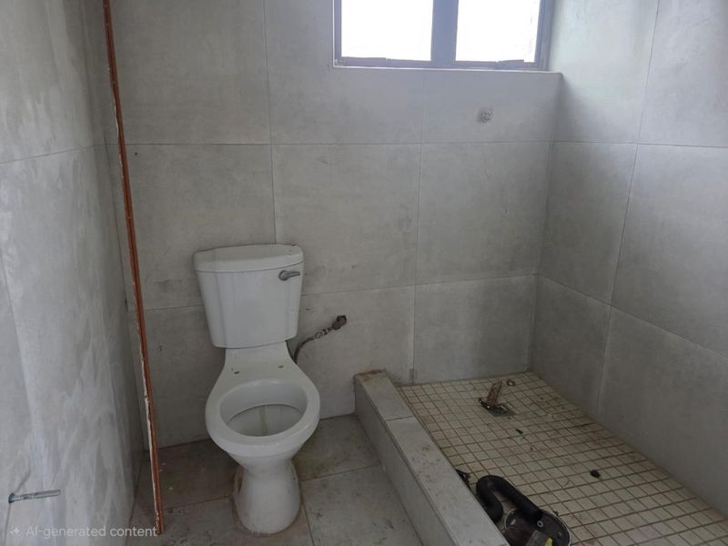 An unfinished bathroom featuring a toilet and a tiled shower base, requiring completion of fixtures and final finishes.