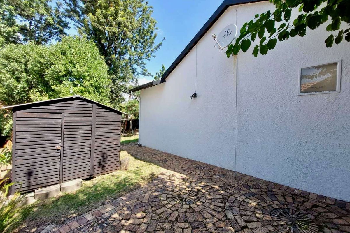 Rear exterior view featuring a paved patio area, a timber garden shed, and a white rendered wall with a satellite dish.