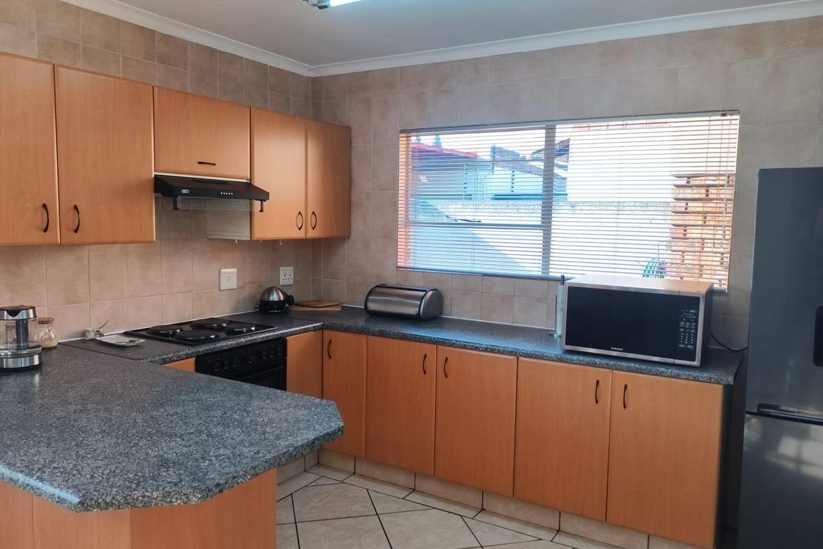 Functional kitchen featuring laminate cabinetry, granite countertops, built-in oven with hob, extractor fan, and tiled finishes throughout.