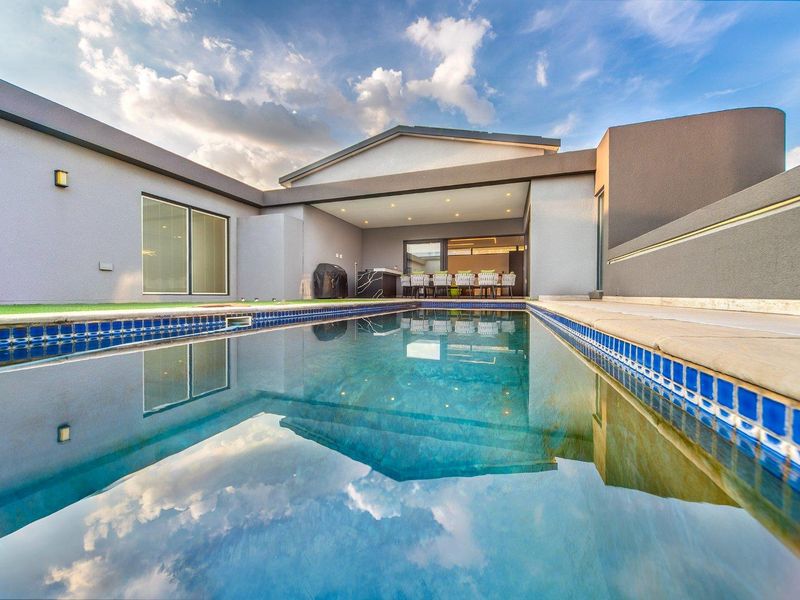 A modern outdoor entertainment area featuring a pristine swimming pool with tiled coping, adjacent to a spacious covered patio with recessed lighting.