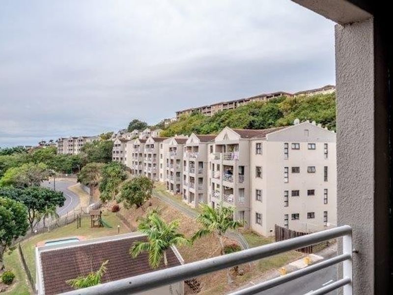 Elevated view from a balcony overlooking the apartment complex grounds, surrounding neighborhood, and lush hillside landscape.