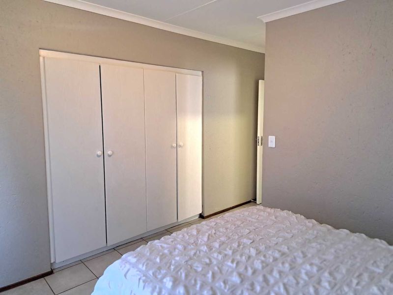 A bedroom featuring neutral wall tones, tiled flooring, and white built-in cupboards providing ample storage space.