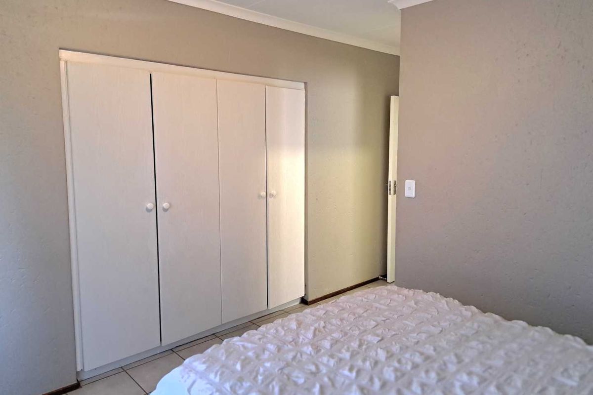 A bedroom featuring neutral wall tones, tiled flooring, and white built-in cupboards providing ample storage space.