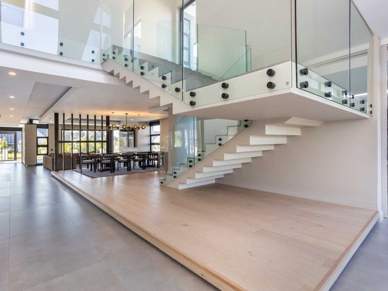 Spacious open-plan living area featuring a modern floating staircase with glass balustrades, high-quality timber and tiled flooring, and contemporary recessed lighting.