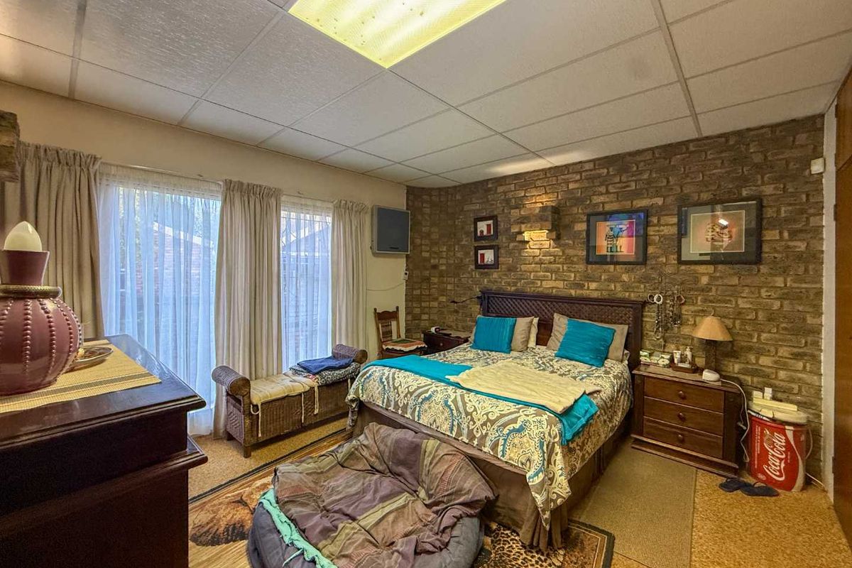 A bedroom featuring an exposed brick feature wall, drop ceiling with integrated lighting, and carpeted flooring.