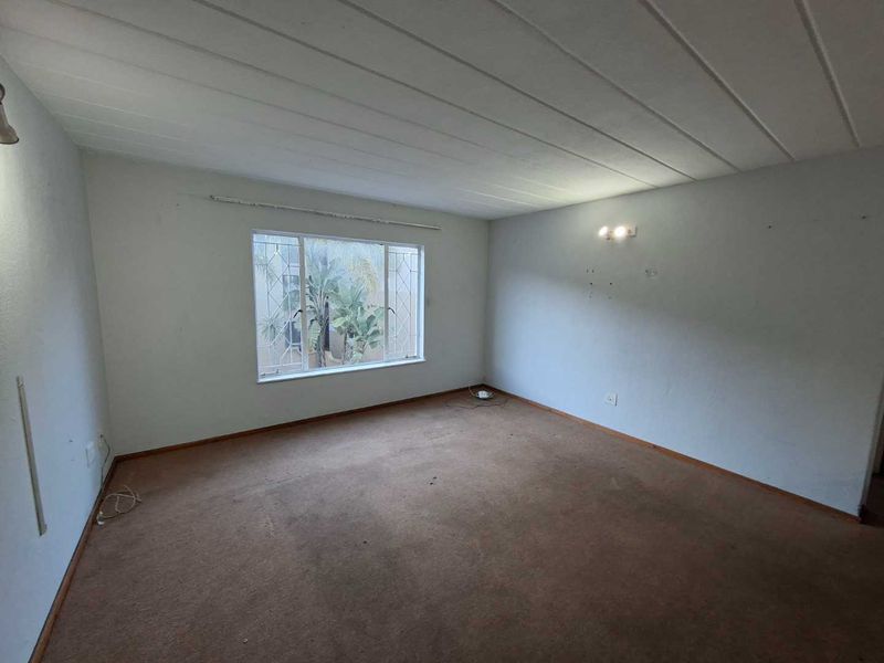 An empty living room featuring carpeted flooring, wall-mounted lighting, and a window with security bars, offering a blank canvas for renovation.