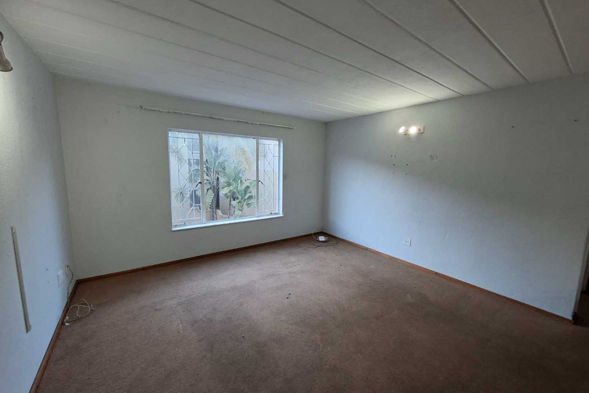 An empty living room featuring carpeted flooring, wall-mounted lighting, and a window with security bars, offering a blank canvas for renovation.