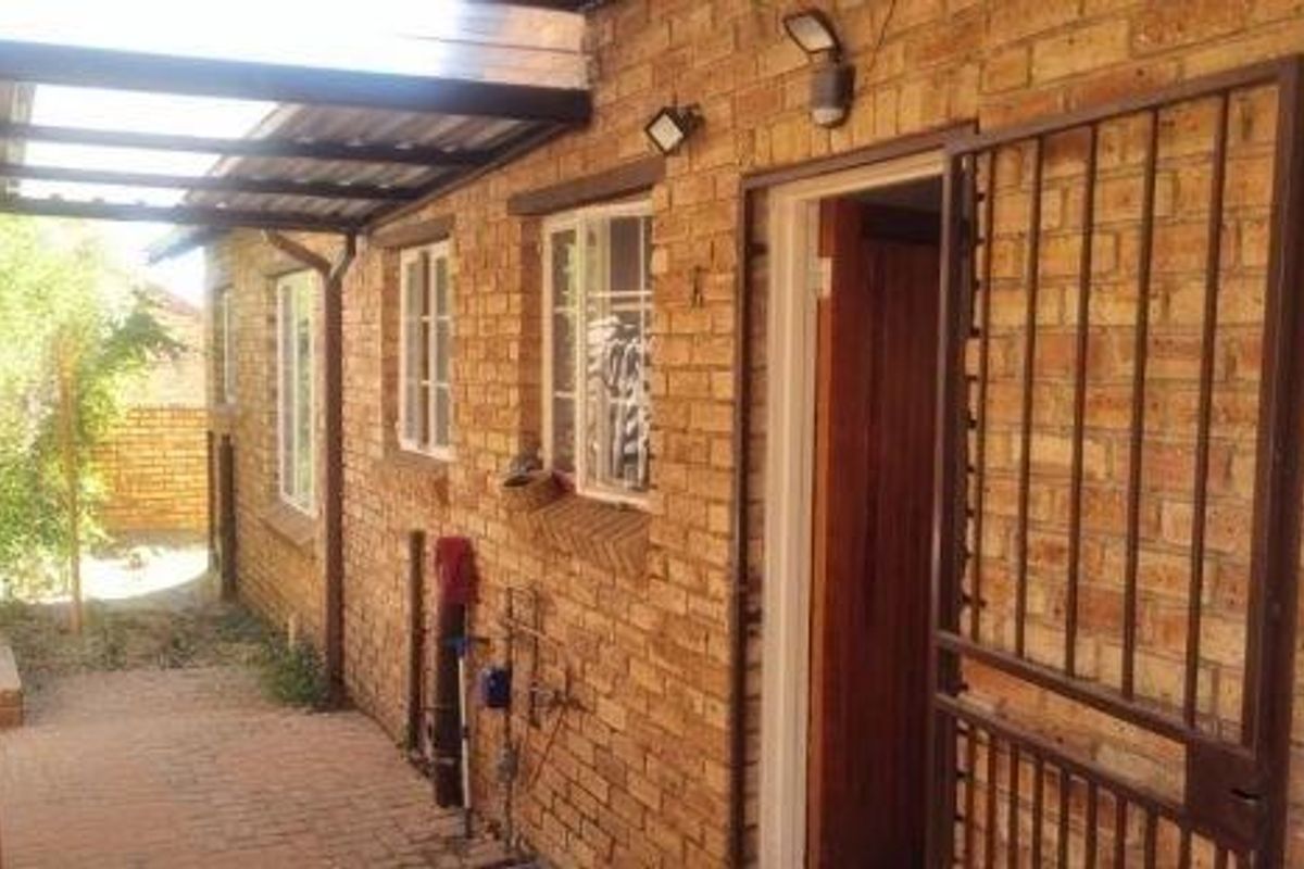 Exterior view of the townhouse side entrance featuring a covered patio area, face-brick facade, and a secure metal gate.