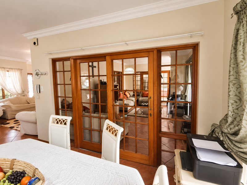 A bright living area featuring classic wooden French doors, terracotta floor tiles, and elegant crown molding, creating a warm and connected living space.